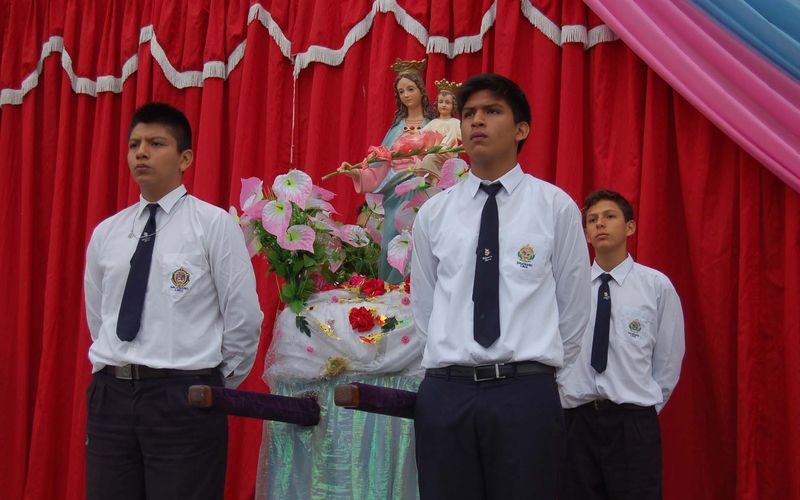Estudiantes con camisa y corbata ofreciendo flores a la imagen de María Auxiliadora