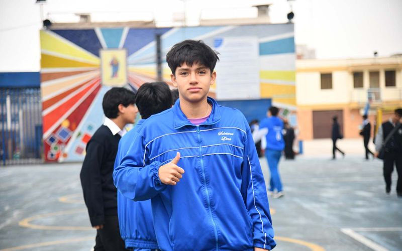 Estudiante de secundaria con buzo azul haciendo gesto de aprobación en el patio