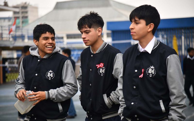 Tres estudiantes de secundaria con casaca sonriendo mientras caminan