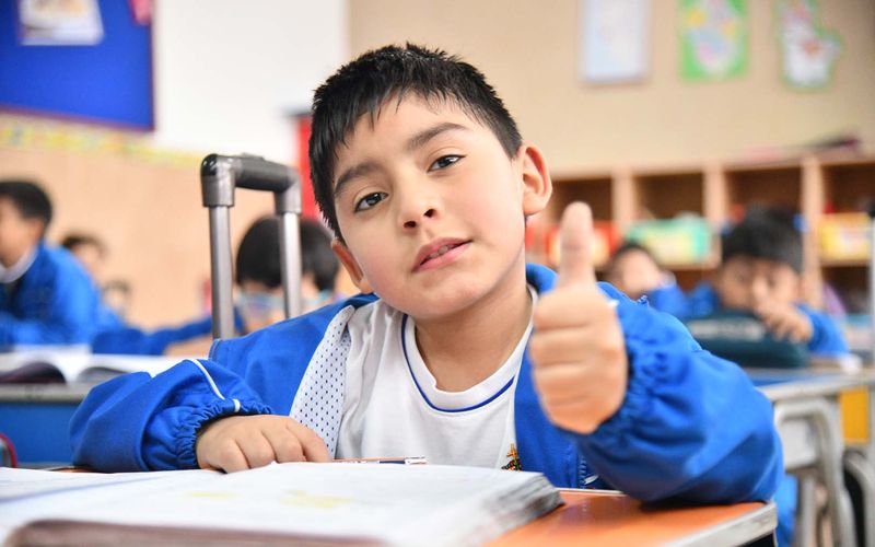 Niño de primaria con el pulgar en alto sentado en su carpeta