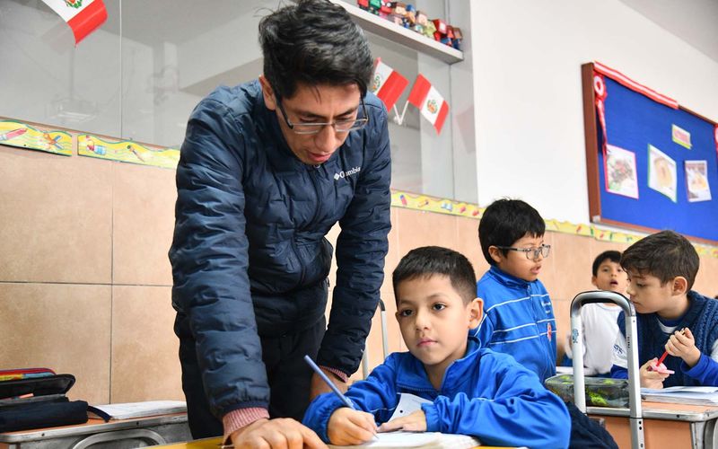 Docente acompañando a un niño de primaria en su carpeta durante la clase