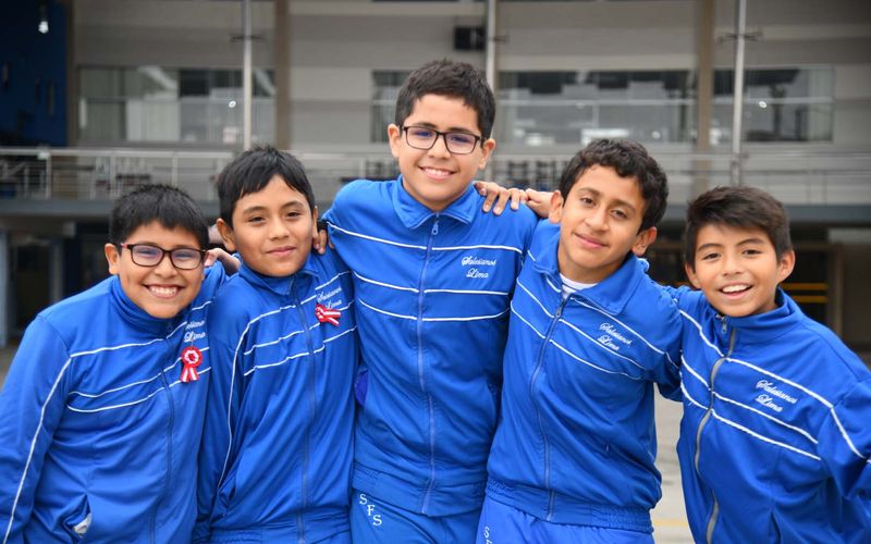 Cinco niños de primaria con buzo azul abrazados y sonrientes en el patio