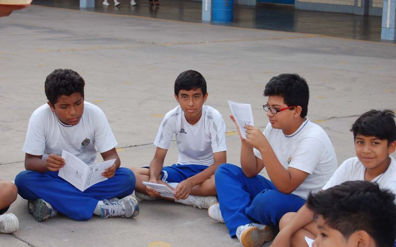 Estudiantes sentados en el patio leyendo hojas en grupo de trabajo