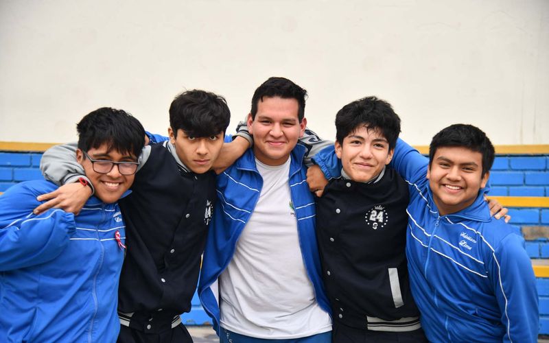 Grupo de estudiantes de secundaria abrazados sonriendo con buzo azul