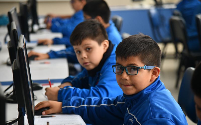 Niños de primaria trabajando en computadoras en el aula