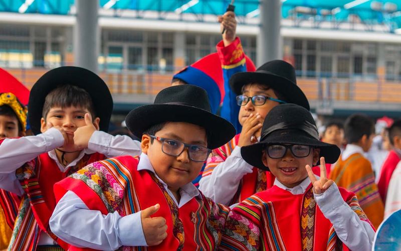 Niños de primaria con ponchos y sombreros de colores en el Día de la peruanidad