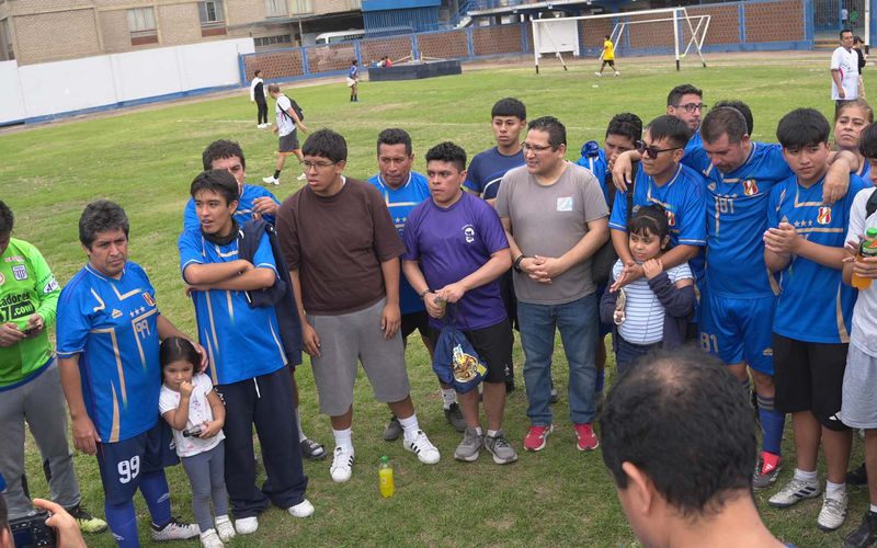 Padres de familia con sus hijos reunidos en círculo sobre la cancha tras el campeonato de fútbol