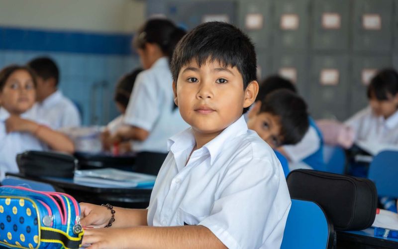 Niño de primaria sonriendo en su carpeta con casilleros al fondo