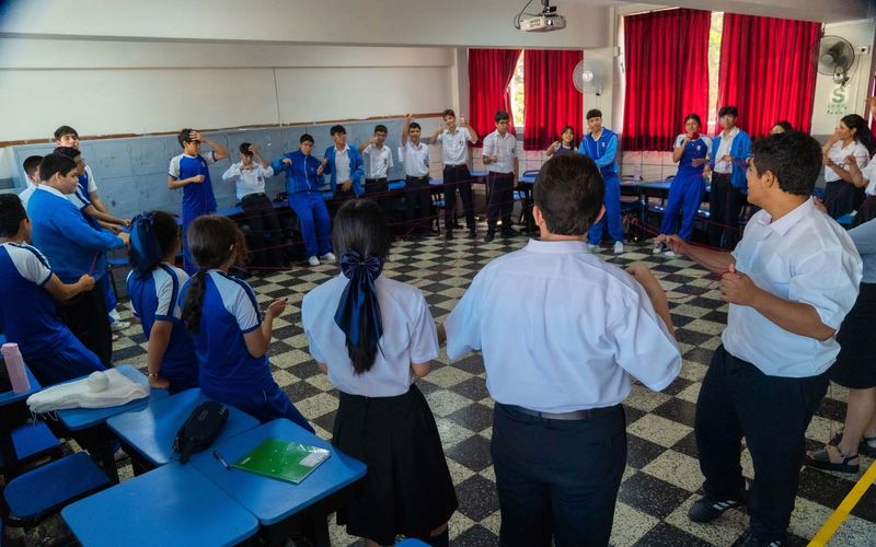 Sesión de tutoría con estudiantes y docente conversando de pie en el aula