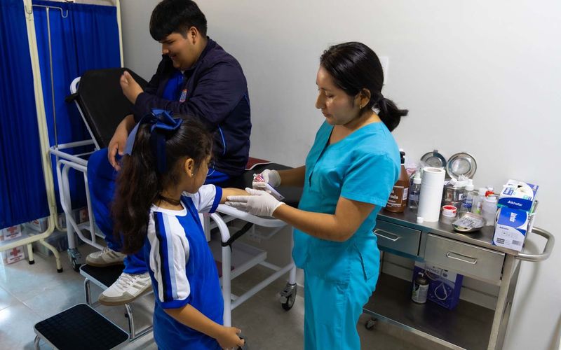 Enfermera atendiendo a una niña de primaria mientras otro estudiante espera