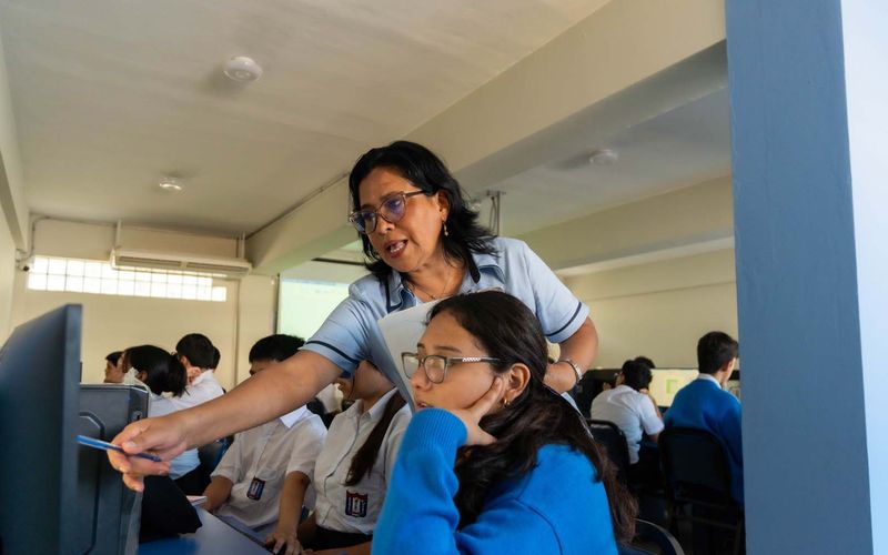 Docente apoyando a una estudiante frente a la computadora