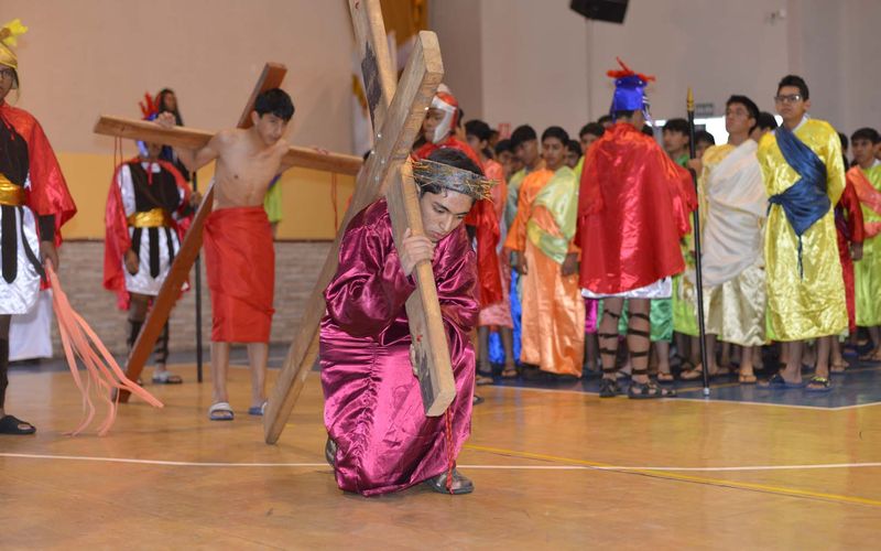 Alumnos con vestuario bíblico en la representación del Vía Crucis; uno de ellos carga la cruz