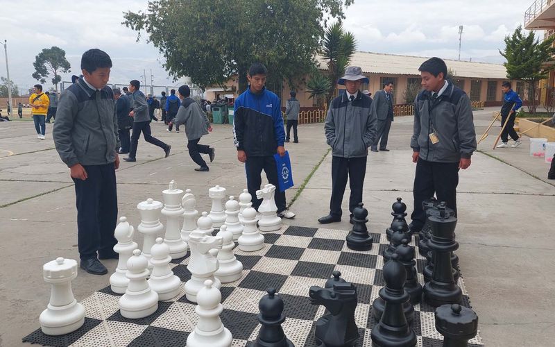 Alumnos y docentes jugando ajedrez con piezas gigantes en el patio