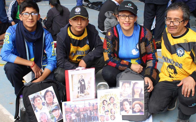 Adultos y jóvenes con polos del colegio sentados en el piso, mostrando retratos y fotos en una actividad de integración