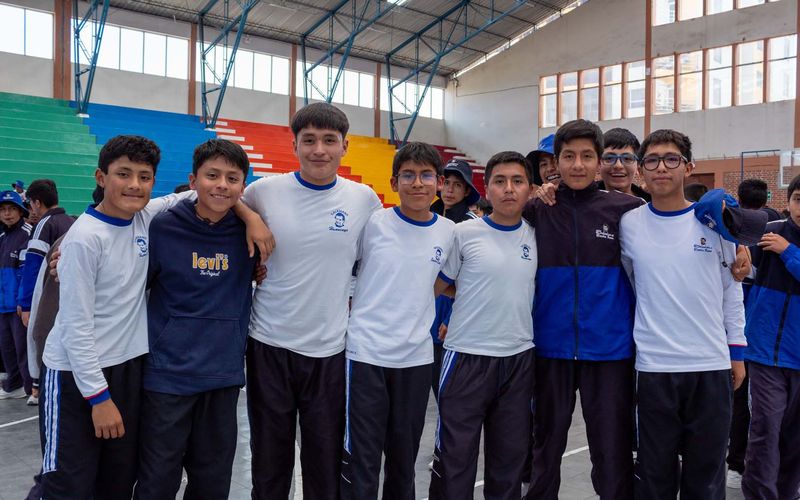 Grupo de alumnos de secundaria con polo blanco posando abrazados en el coliseo