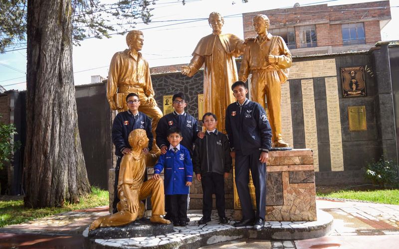Alumnos junto al conjunto escultórico dorado de Don Bosco y los jóvenes en el patio