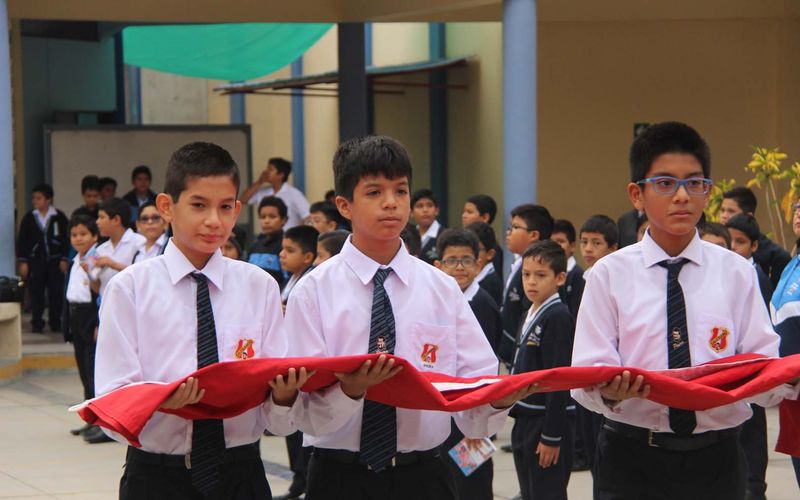 Tres alumnos portando la bandera del Perú durante una ceremonia cívica