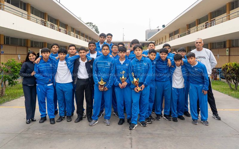 Equipo deportivo de secundaria con buzos azules sosteniendo trofeos junto a sus docentes