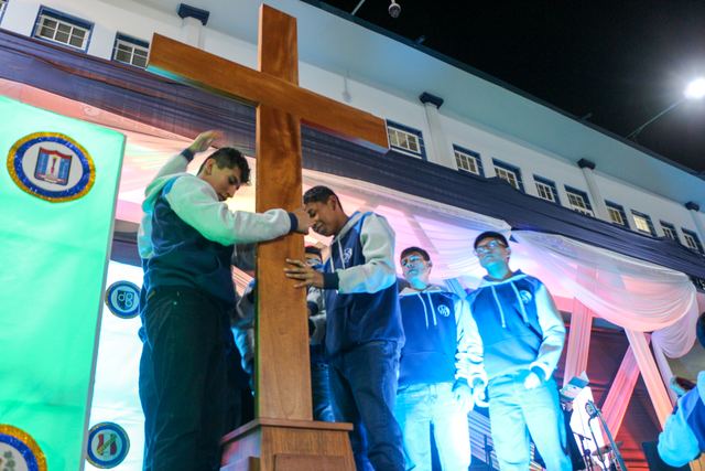 Jóvenes sostienen una cruz de madera sobre un escenario iluminado de noche