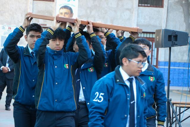 Estudiantes con chaquetas azules llevan una cruz de madera sobre los hombros