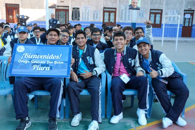 Estudiantes de Piura sentados con el letrero de bienvenida de su colegio