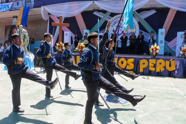 Jóvenes de una escolta marchan frente al escenario con banderas
