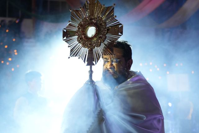 Sacerdote sostiene la custodia con el Santísimo entre humo de incienso durante la adoración