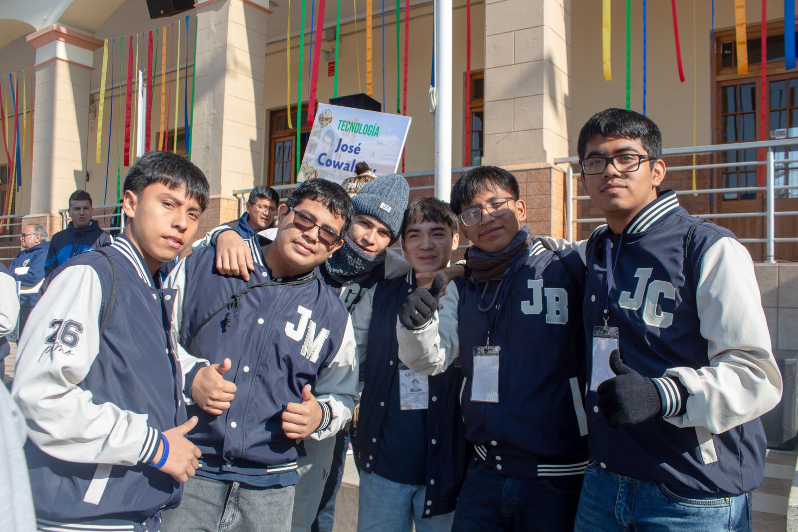 Estudiantes con chaquetas de promoción posan con el pulgar en alto frente al letrero del taller de tecnología