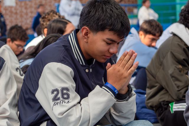Un joven con chaqueta de promoción reza con las manos juntas