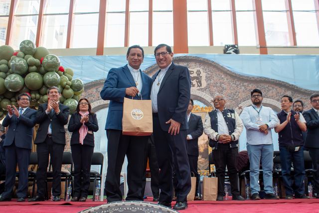 Dos hombres se saludan y entregan un obsequio en el escenario durante la clausura